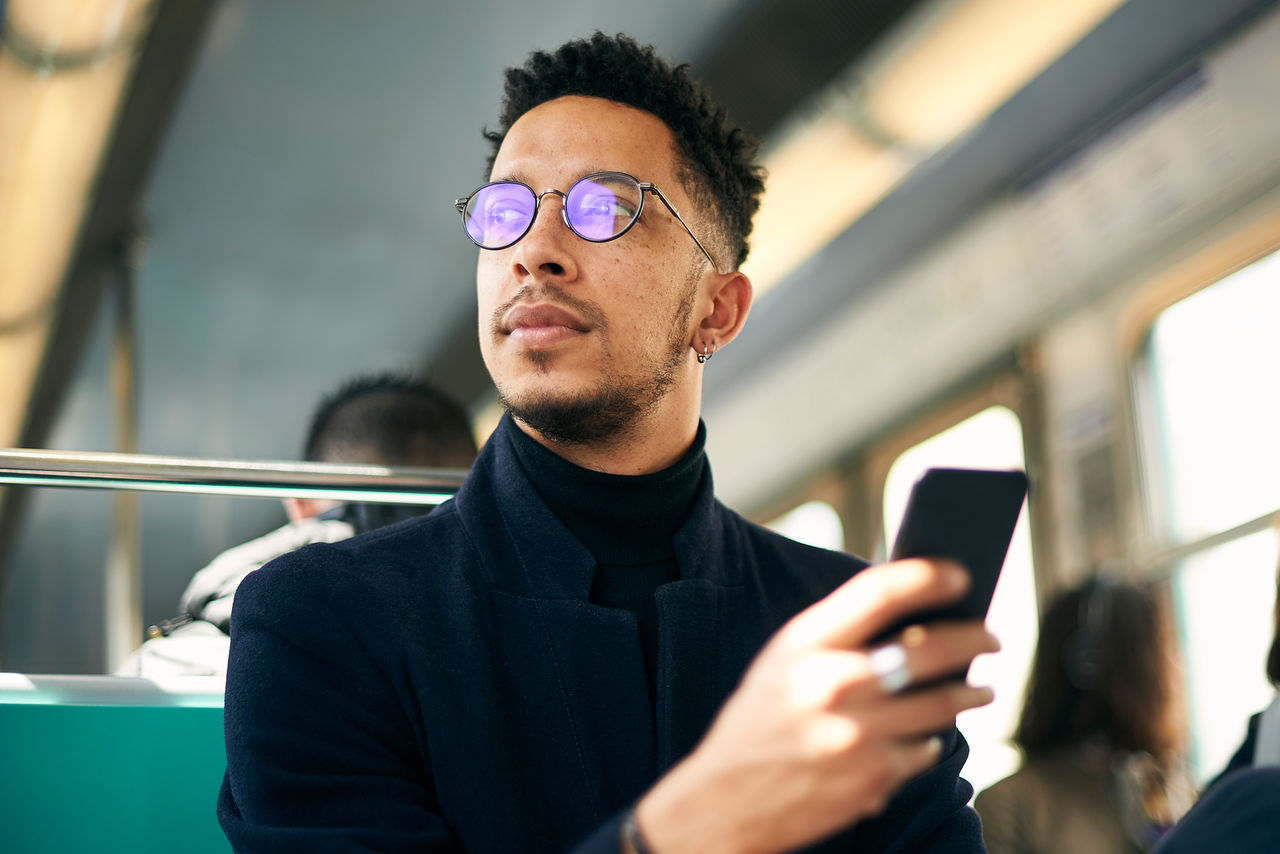 Thoughtful businessman holding smartphone while sitting in train